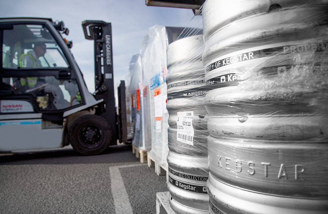 A truck lifting up some boxes, with kegs in the foreground.